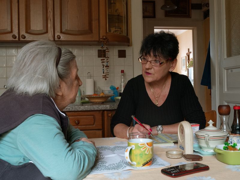 An older woman and a carer chatting at the kitchen table