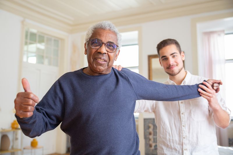 An older man laughing with a young carer at home