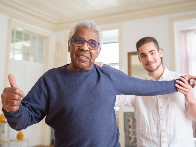 An older man laughing with a young carer at home
