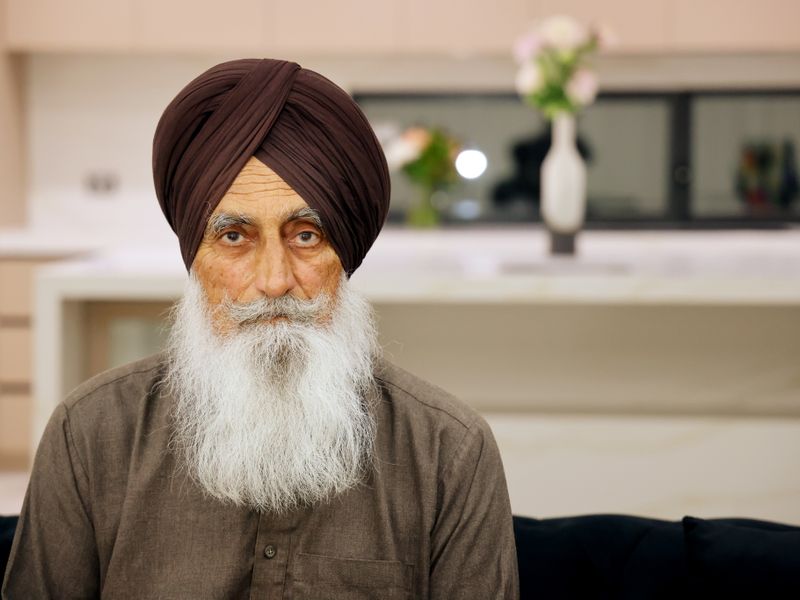 An older man wearing a turban, sitting in his living room