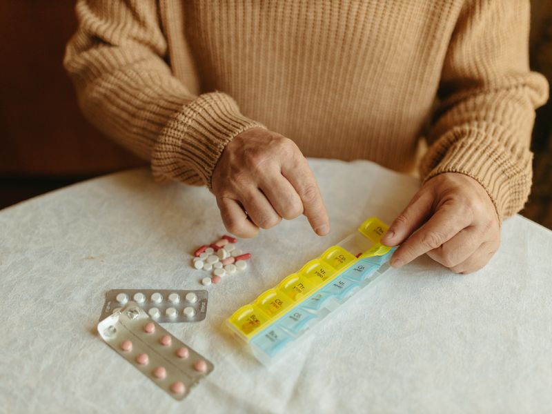 An older person sorting their own tablets into a weekly pill organiser